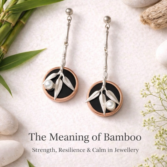 Pair of earrings with bamboo design on a textured surface with leaves and stones.
