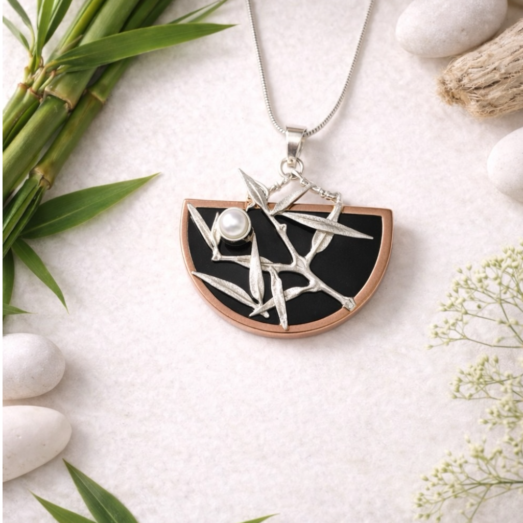Japanese style Necklace with a black and silver pendant on a white surface with bamboo and flowers.