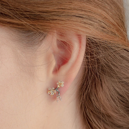 Handmade sterling silver almond blossom branch stud earrings with gold-plated details and rose gemstone accents worn on the ear.