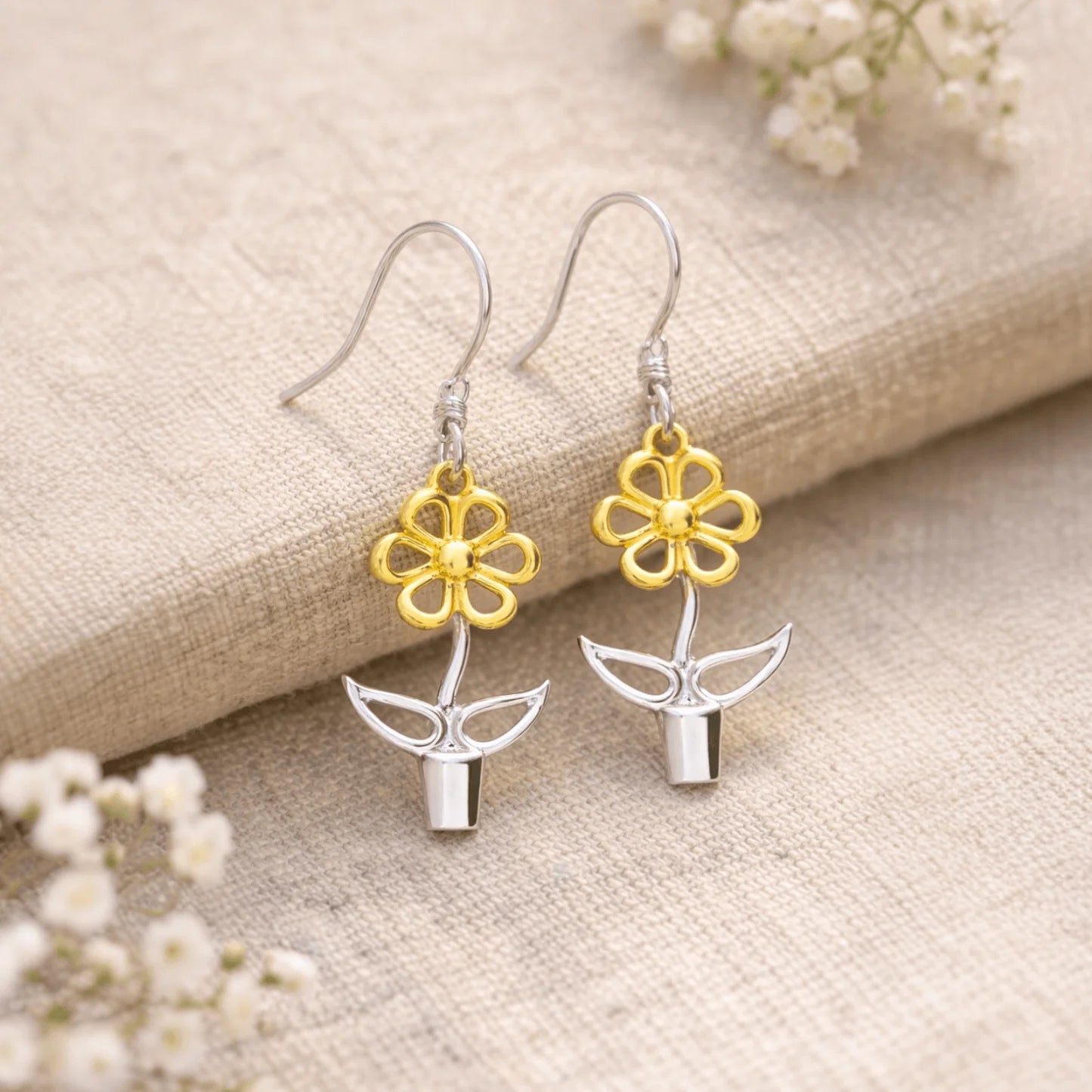 Sterling silver and gold Blooming Joy flower pot drop earrings styled on natural linen with delicate botanical details