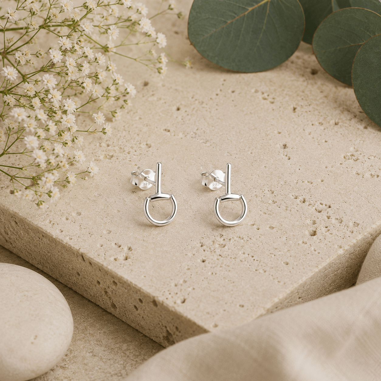 Mini sterling silver snaffle stud earrings styled on natural stone with botanical details and soft neutral textures