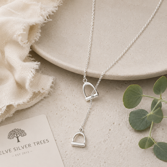 Small sterling silver stirrup drop necklace styled on natural stone with botanical accents