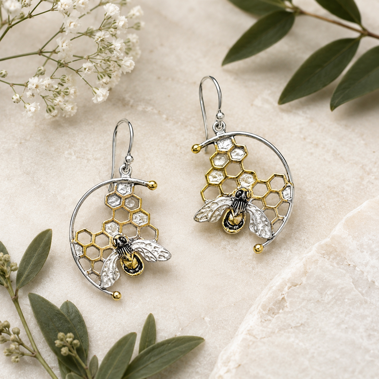 Sterling silver honeycomb bee hook earrings with gold vermeil accents styled on natural stone with botanical foliage.