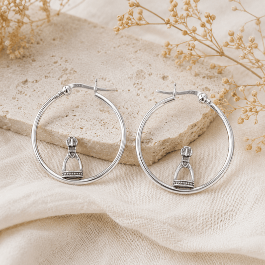 Sterling silver stirrup hoop earrings styled on natural stone and soft linen in a luxury equestrian inspired flatlay