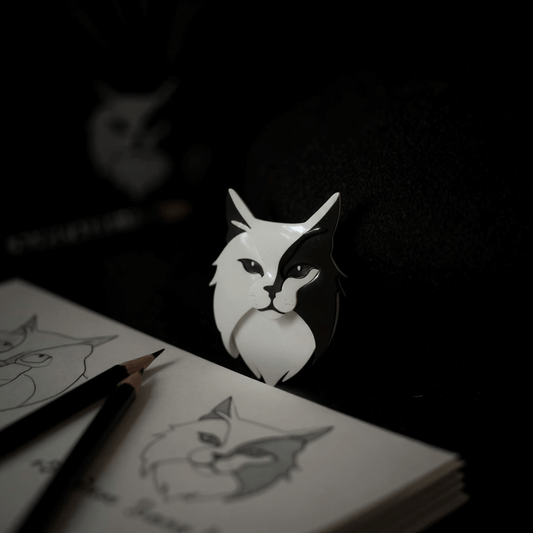 Image of a an acrylic art brooch of a cat behind a an artists sketch book
