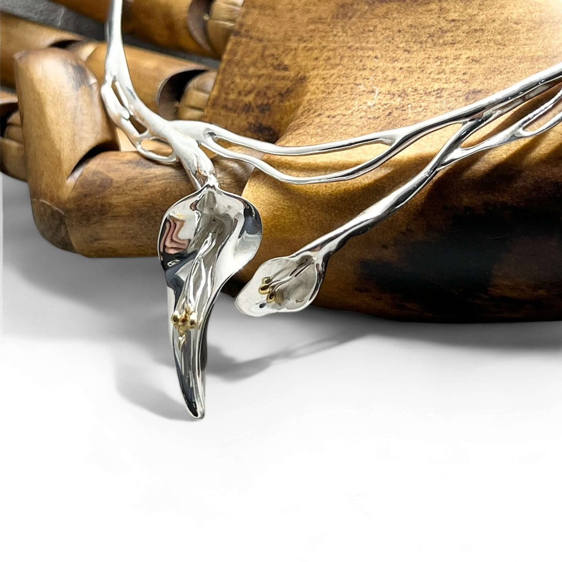 Statement calla lily necklace handmade in 925 sterling silver with 18 carat gold accents. The necklace features 2 flowers on an organic high shine panel, presented against a life size artist wooden hand for scale. 