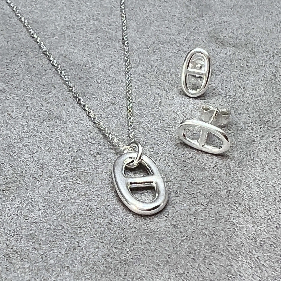 Hidden Symbolism - The Anchor Link Charm In Jewellery blog post cover image featuring a sterling silver mariner link pendant and earrings on a grey suede background from twelve silver trees jewellery and gifts