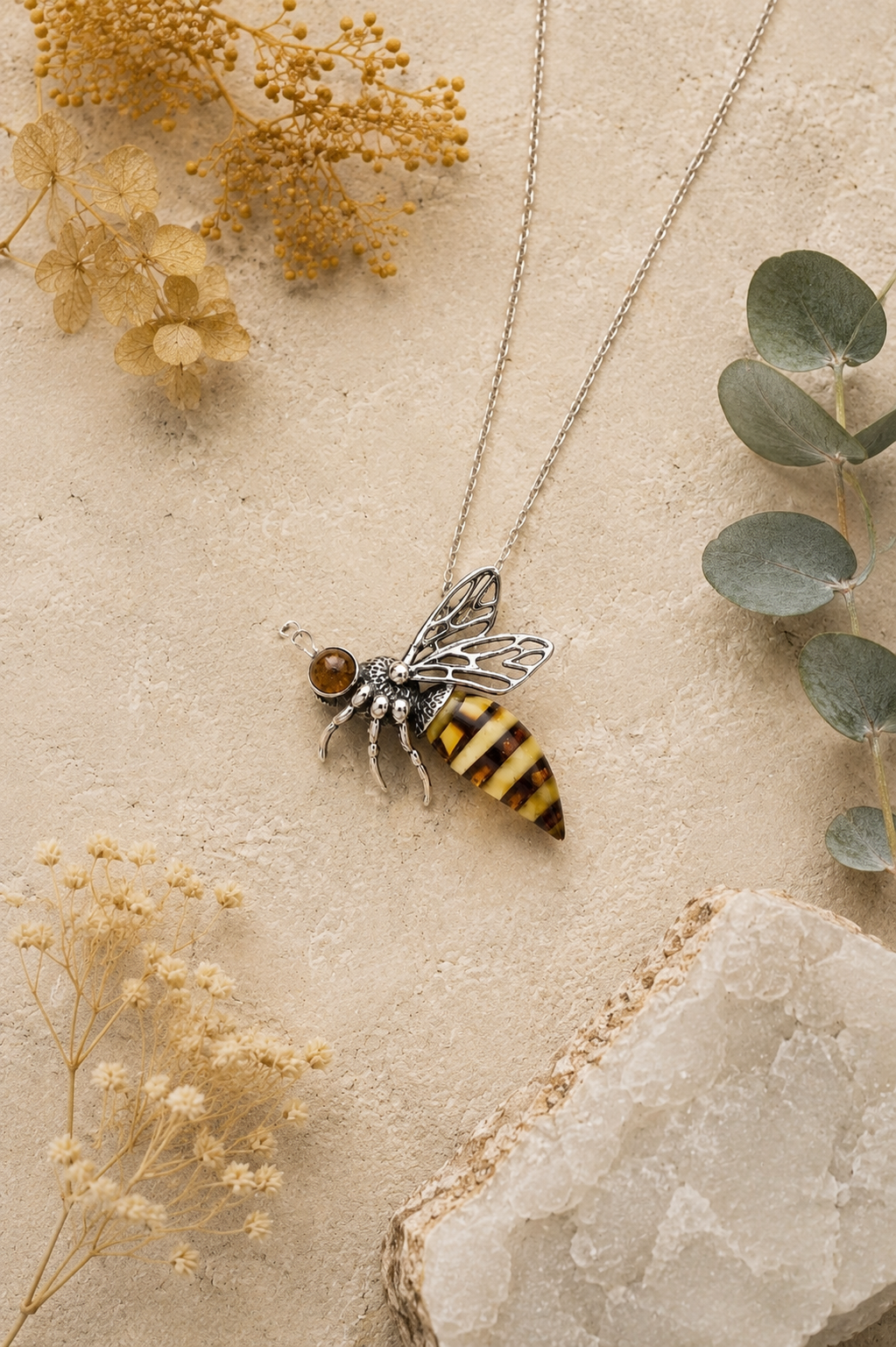 Sterling silver Baltic amber bee pendant styled on natural stone with dried botanicals and soft neutral tones