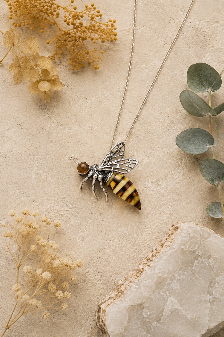 Sterling silver Baltic amber bee pendant styled on natural stone with dried botanicals and soft neutral tones