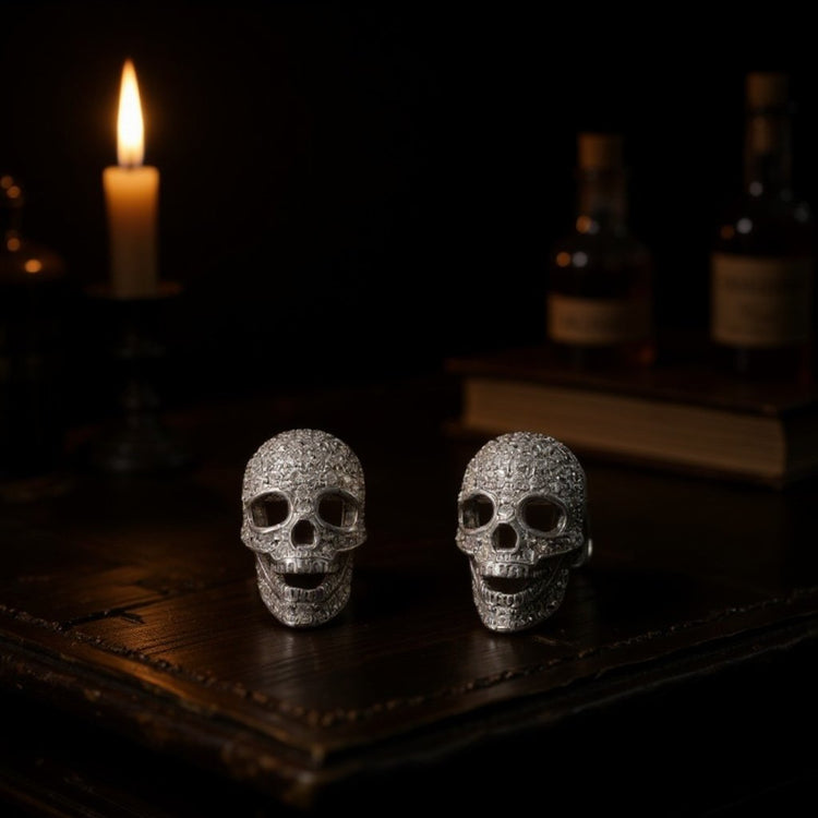 Image of three dimensional sterling silver skull stud earrings set sparkling cubic zirconias on a dark wooden table with a candle on the background 