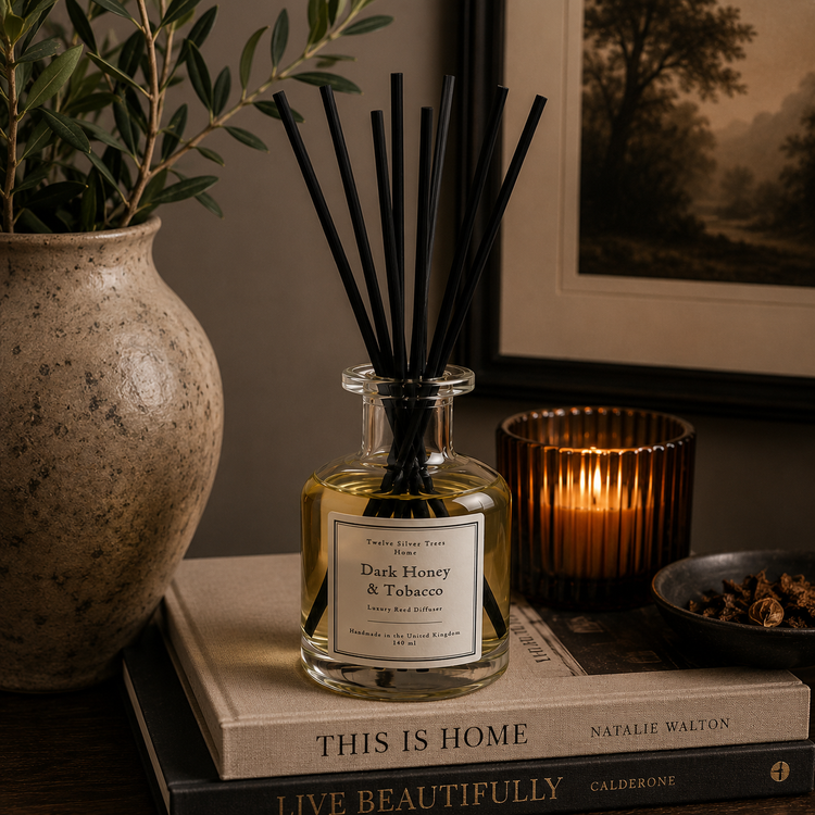 Dark Honey & Tobacco reed diffuser styled on interior design books with candlelight and natural home décor accents. Cover image for Twelve Silver Trees Jewellery luxury home fragrance collection 