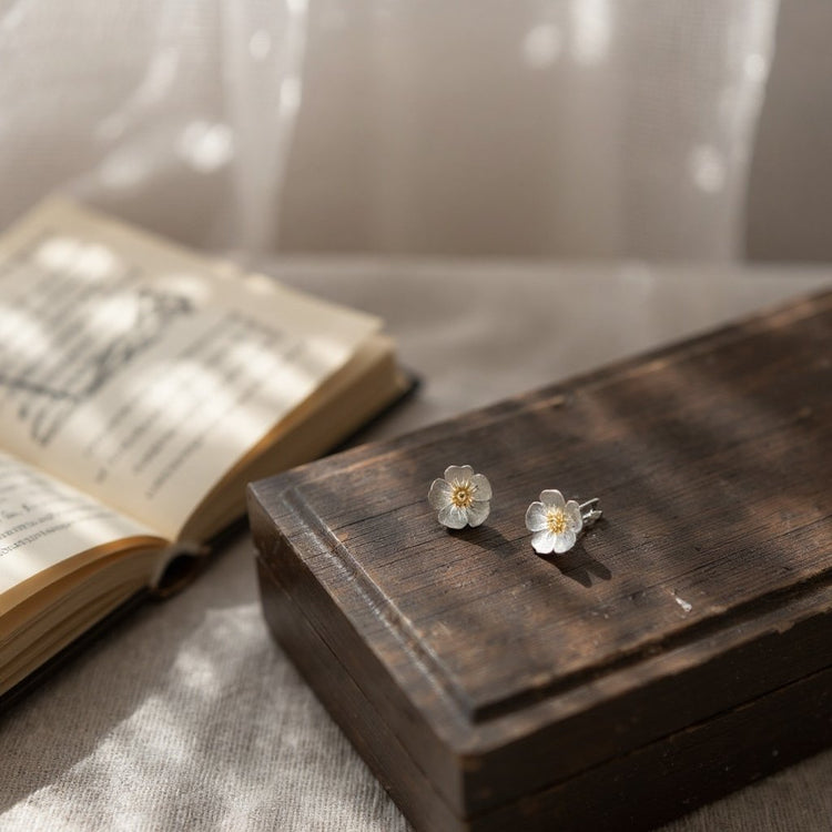 Image of handmade sterling silver and 18 carat gold buttercup stud earrings displayed on a vintage wooden chest 