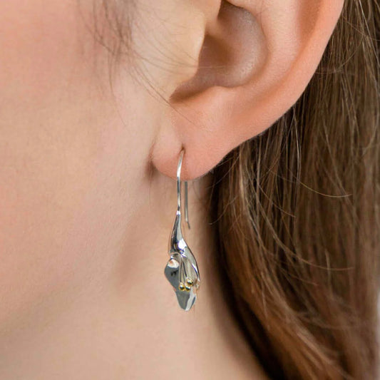 Close-up of a person wearing sterling silver calla lily flower earrings with a blurred background