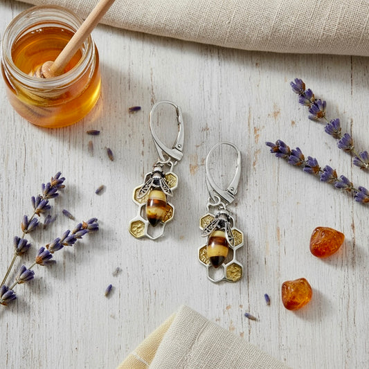 Pair of silver earrings with amber stones on a wooden surface with honey and lavender.