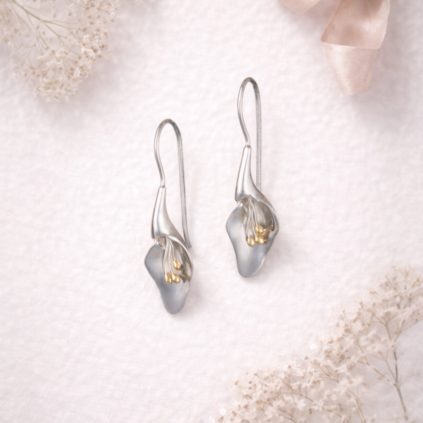from the herbarium collection at Twelve Silver Trees Jewellery , Silver calla lily earrings on a soft white background with delicate flowers.