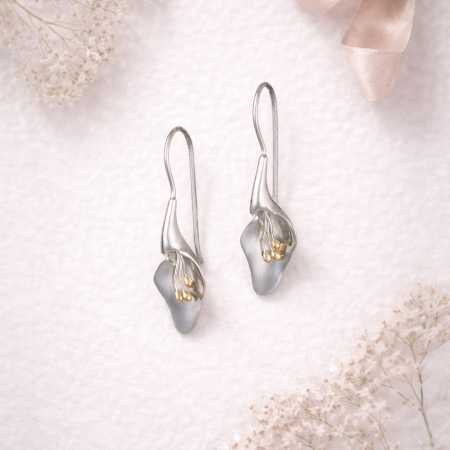 from the herbarium collection at Twelve Silver Trees Jewellery , Silver calla lily earrings on a soft white background with delicate flowers.