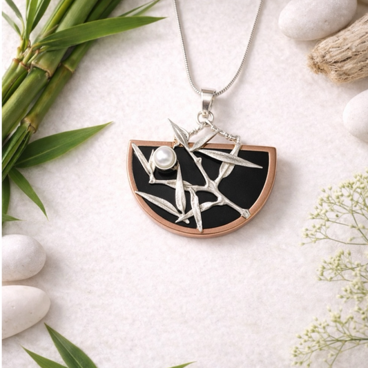 Japanese style Necklace with a black and silver pendant on a white surface with bamboo and flowers.