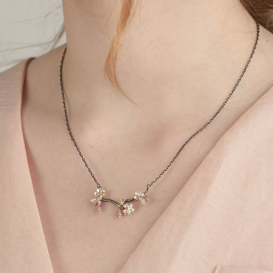 Handmade sterling silver almond blossom branch necklace with gold-plated blossom details and rose gemstone  accents worn by a model.