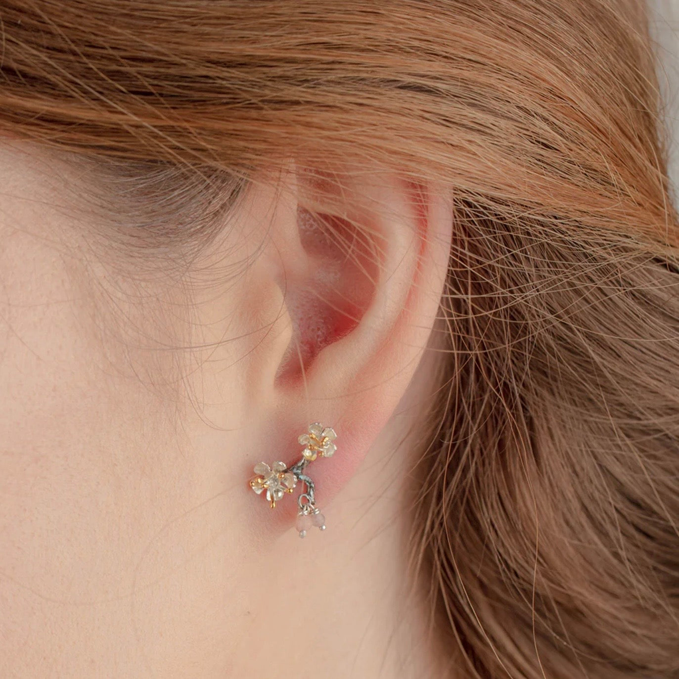Handmade sterling silver almond blossom branch stud earrings with gold-plated details and rose gemstone accents worn on the ear.