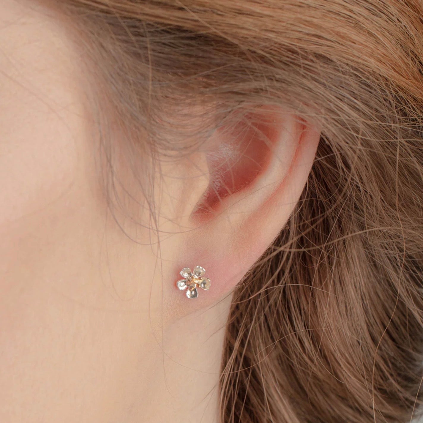 Handmade sterling silver almond blossom flower stud earrings with gold-plated details worn on the ear.