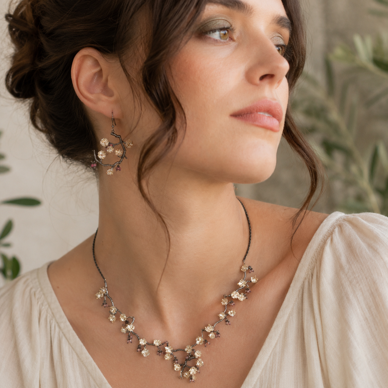Handmade sterling silver almond blossom statement necklace and matching hoop earrings with gold-plated blossom details worn with an ivory blouse.