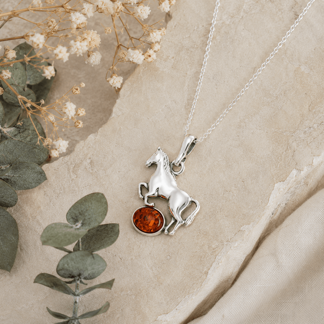 Sterling silver horse pendant necklace with amber gemstone styled on natural stone with eucalyptus and dried flowers