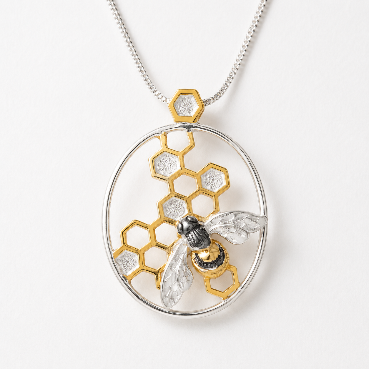 Close-up of handmade sterling silver bee pendant with gold vermeil honeycomb and black rhodium detailing suspended from a sterling silver chain.
