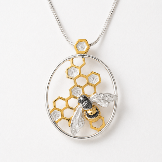 Close-up of handmade sterling silver bee pendant with gold vermeil honeycomb and black rhodium detailing suspended from a sterling silver chain.