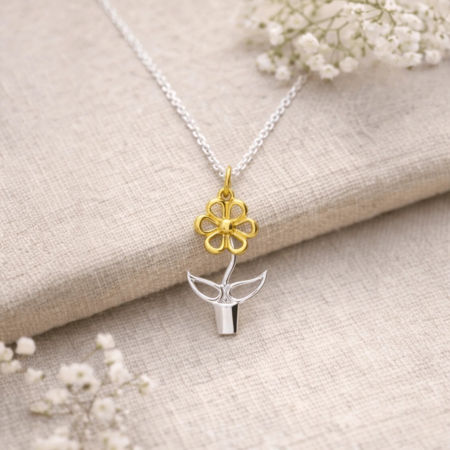 Blooming Joy flower pot pendant necklace in sterling silver and gold styled on natural linen with soft white flowers