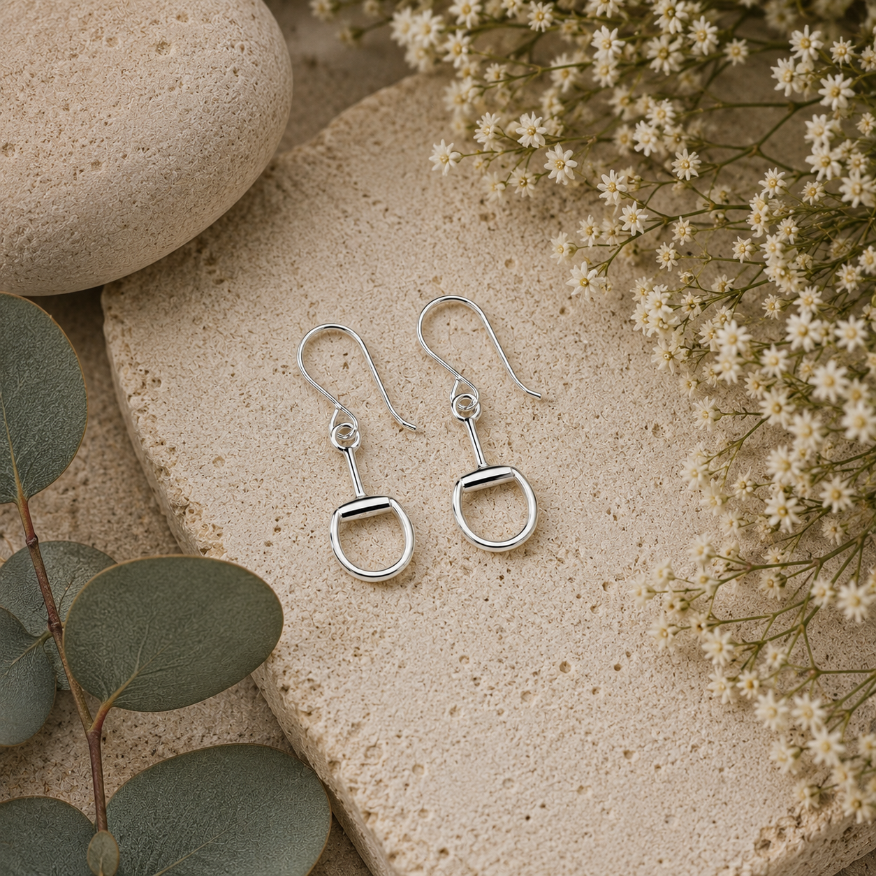 Sterling silver snaffle bit hook earrings styled on natural stone with botanical flowers and eucalyptus leaves