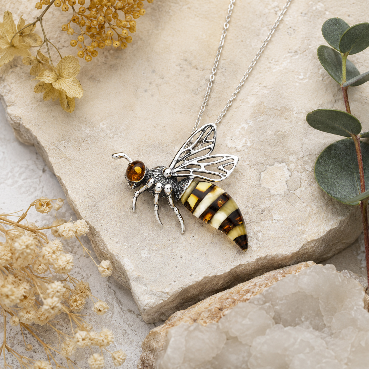 Sterling silver Baltic amber bee pendant styled on natural stone with botanical details