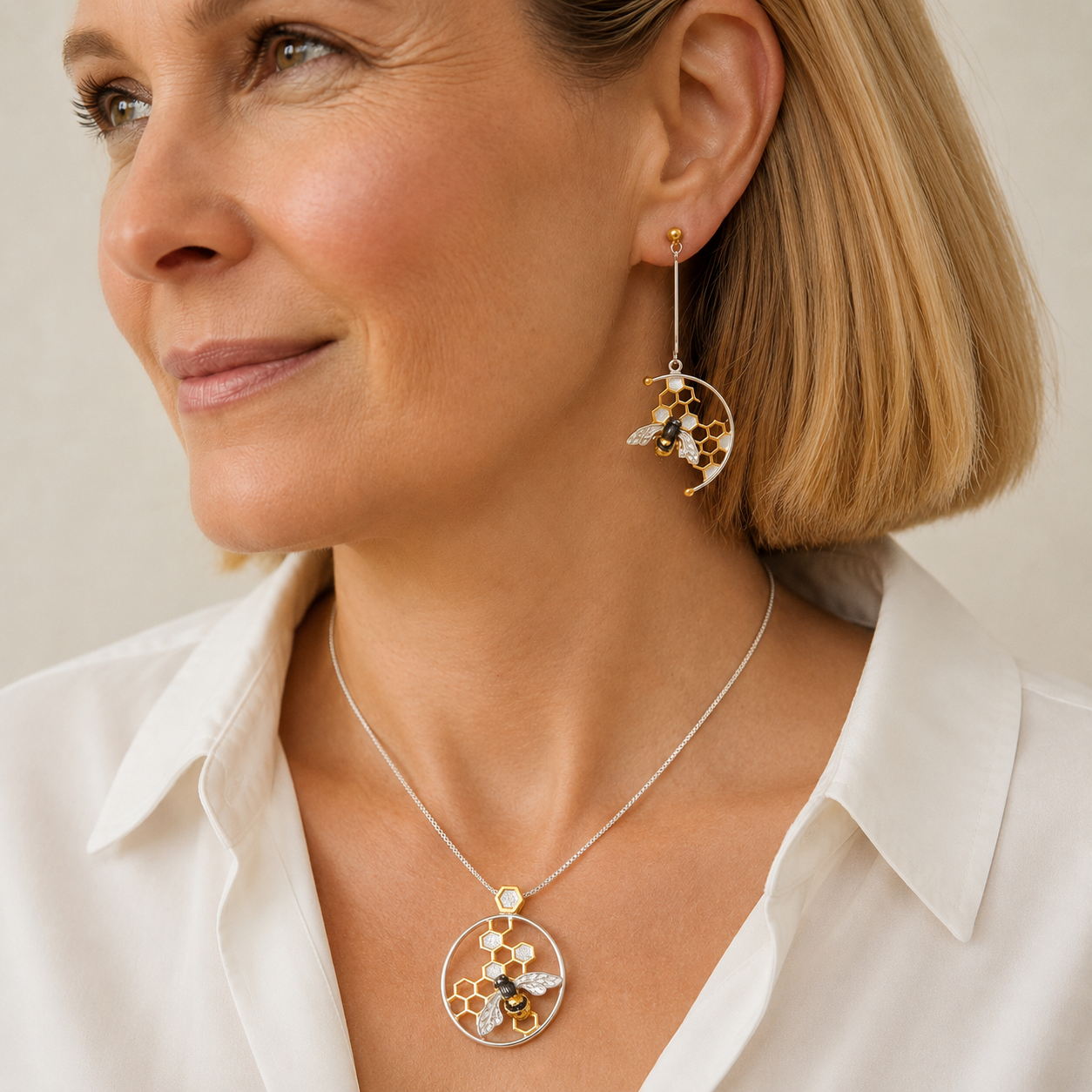 Woman wearing matching honeycomb and honeybee sterling silver pendant necklace and long drop earrings with gold detailing.