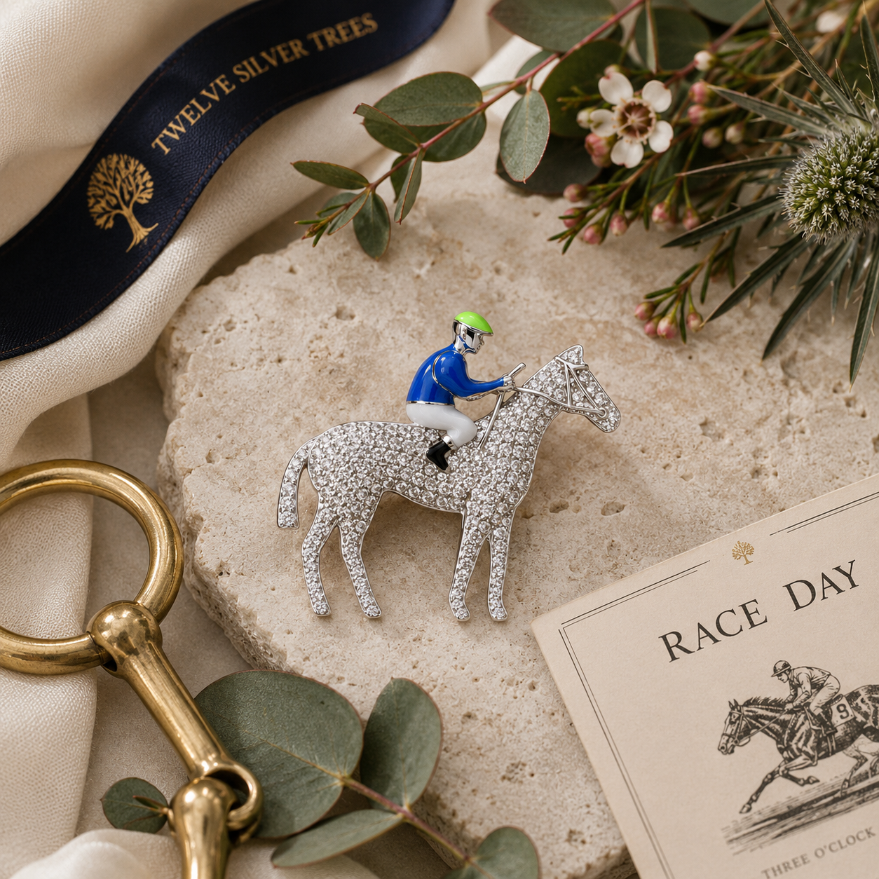 Horse and jockey pavé sterling silver brooch styled with leather gloves, race card and brass snaffle in luxury equestrian flat lay