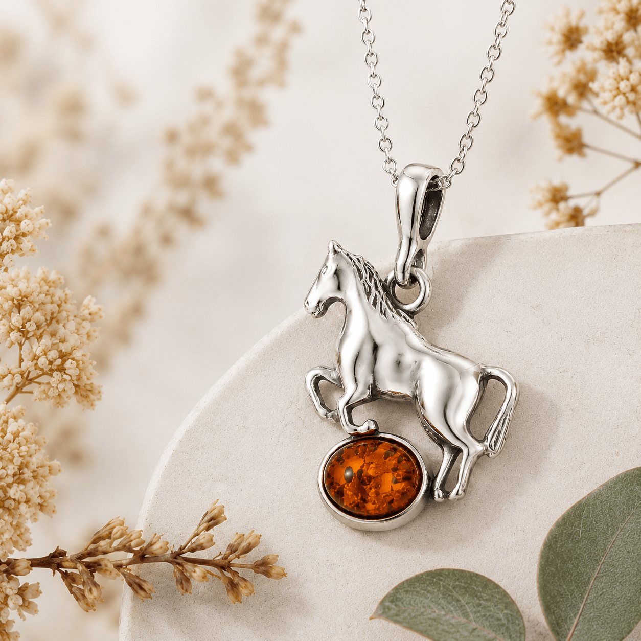 Close-up of sterling silver horse pendant necklace with amber gemstone styled with soft botanical accents and neutral stone textures
