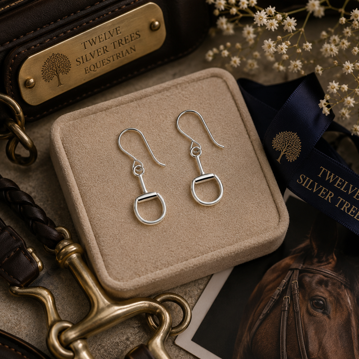 Sterling silver snaffle bit hook earrings styled on a luxury equestrian-inspired flat lay with leather and brass accents