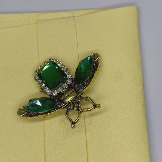 Vintage style rhinestone bee brooch in an antique gold tone finish with a large central green rhinstone surrounded by a halo of of sparkling clear stones.