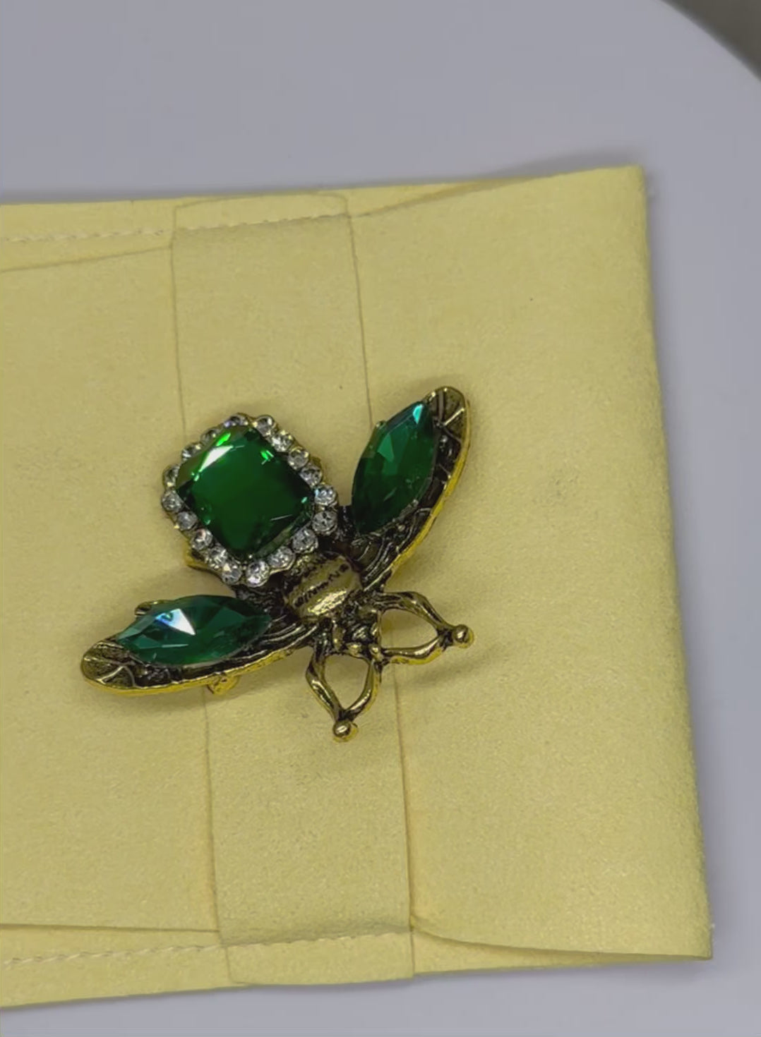 Vintage style rhinestone bee brooch in an antique gold tone finish with a large central green rhinstone surrounded by a halo of of sparkling clear stones.