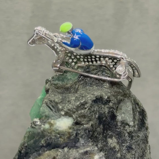 Video of Stunning antique inspired hand crafted sterling silver brooch of a horse & jockey. The horse is covered in pave-set high carbon zirconia gemstones while the jockey is enamelled in blue and white. Displayed on an uncut raw emerald boulder 