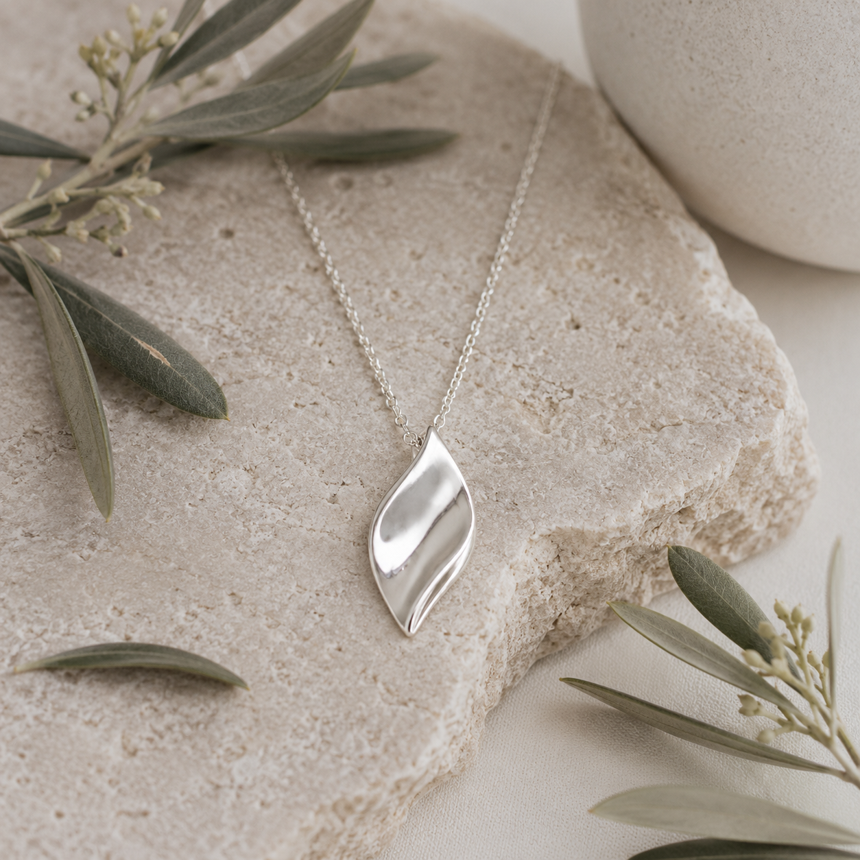 Sculpted leaf sterling silver pendant necklace styled on natural stone with soft botanical olive branches