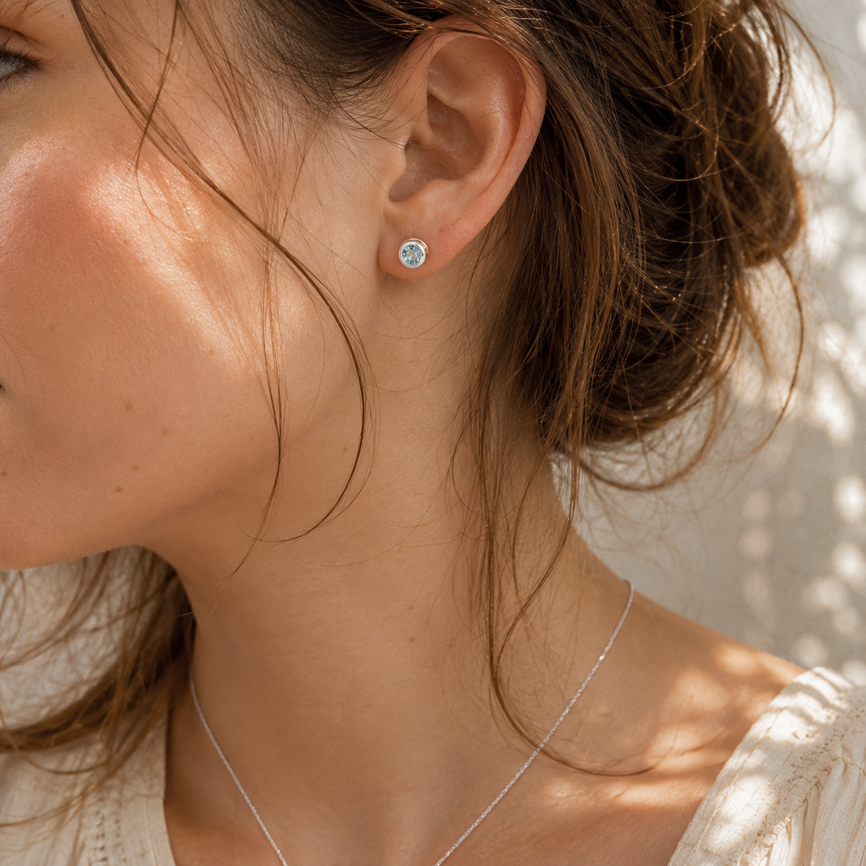 Small handcrafted Sky Blue Topaz stud earrings worn in the ear with sterling silver and gold detailing