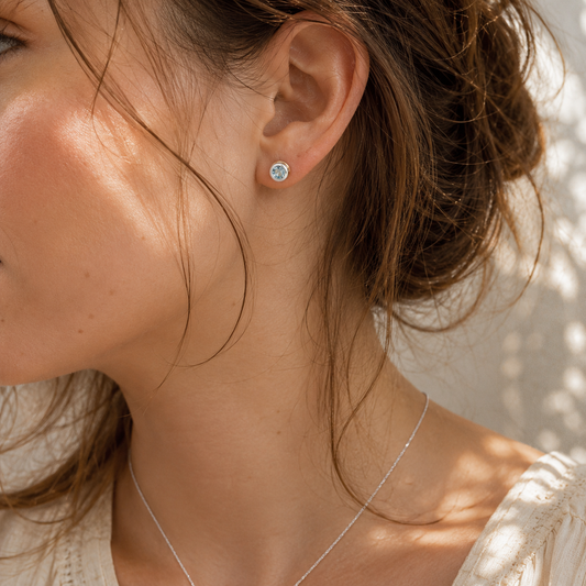 Small handcrafted Sky Blue Topaz stud earrings worn in the ear with sterling silver and gold detailing