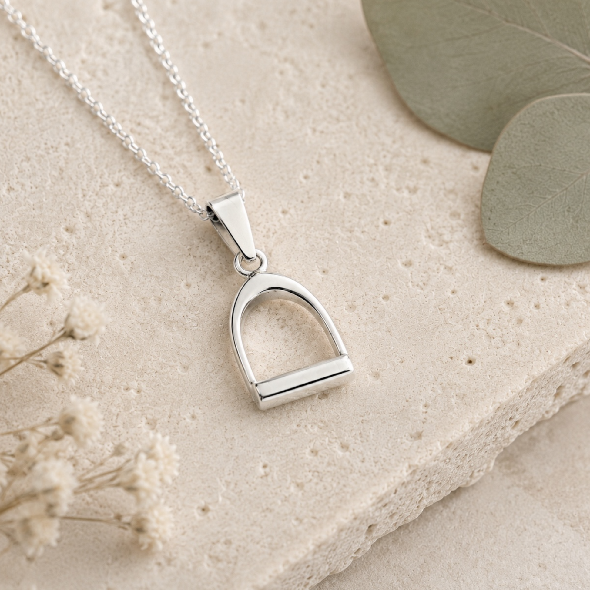 Small sterling silver stirrup pendant necklace on limestone stone with eucalyptus and botanical styling