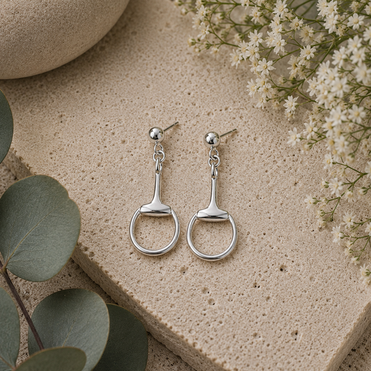 Sterling silver snaffle drop earrings styled on natural stone with eucalyptus and white flowers