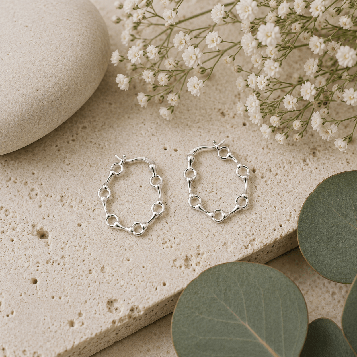 Sterling silver snaffle hoop earrings displayed on natural stone with botanical styling and soft earthy tones