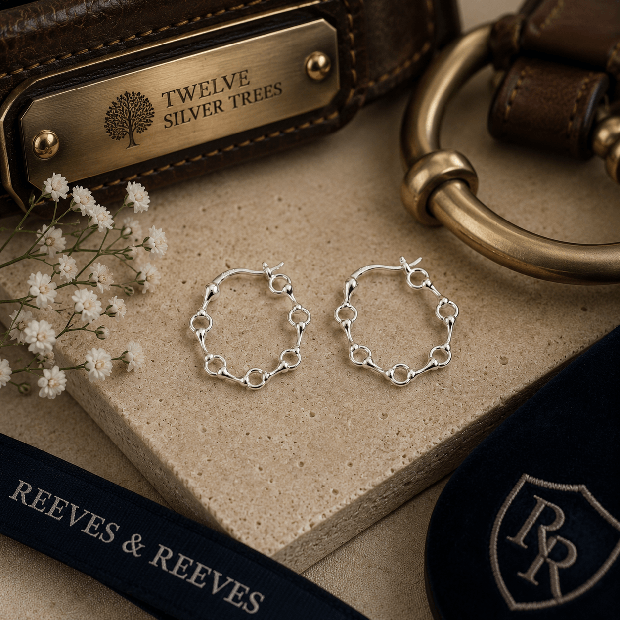 Sterling silver snaffle hoop earrings styled with luxury equestrian leather accessories and warm neutral textures