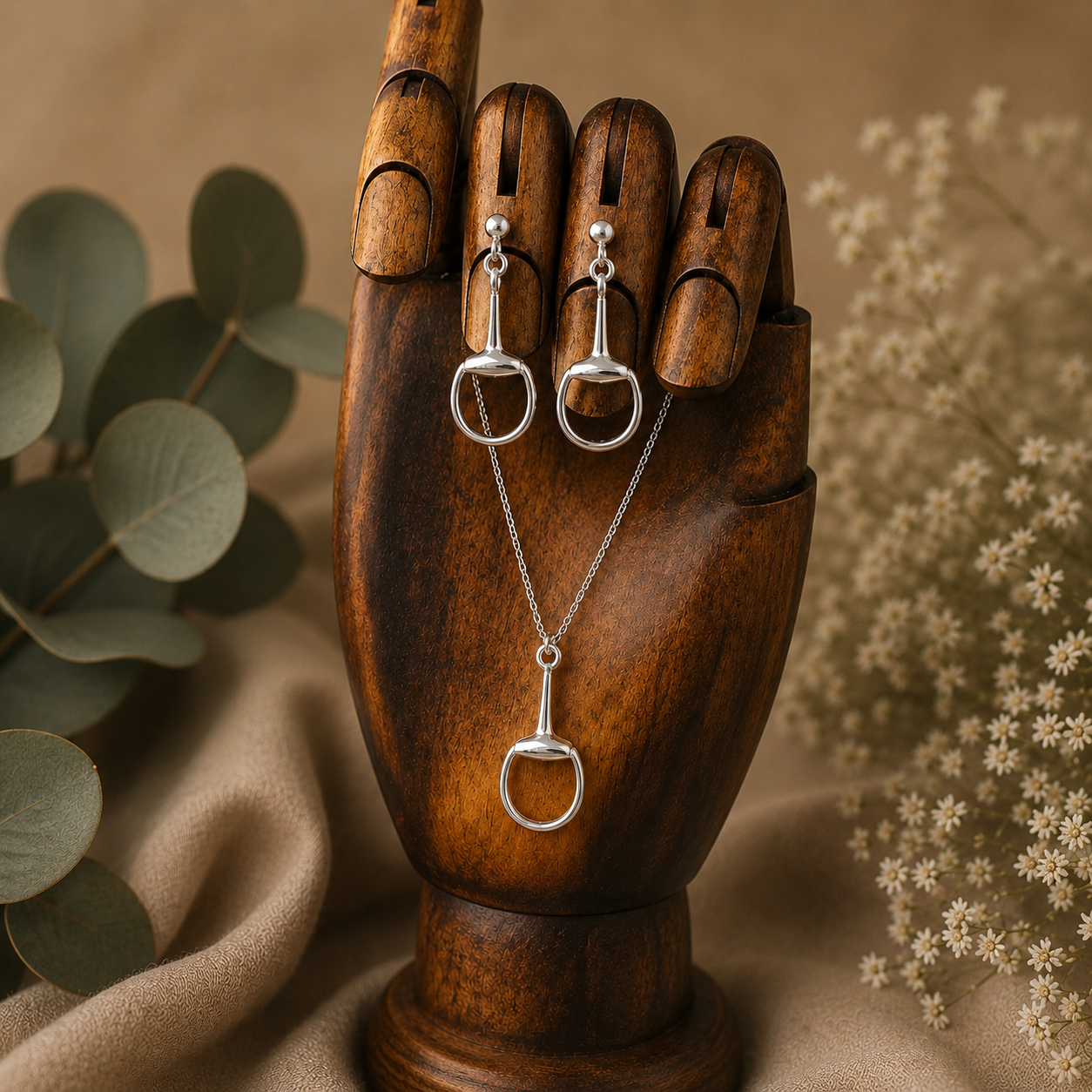 Sterling silver snaffle pendant necklace and matching drop earrings displayed on a wooden artist’s hand with soft botanical styling and neutral luxury background