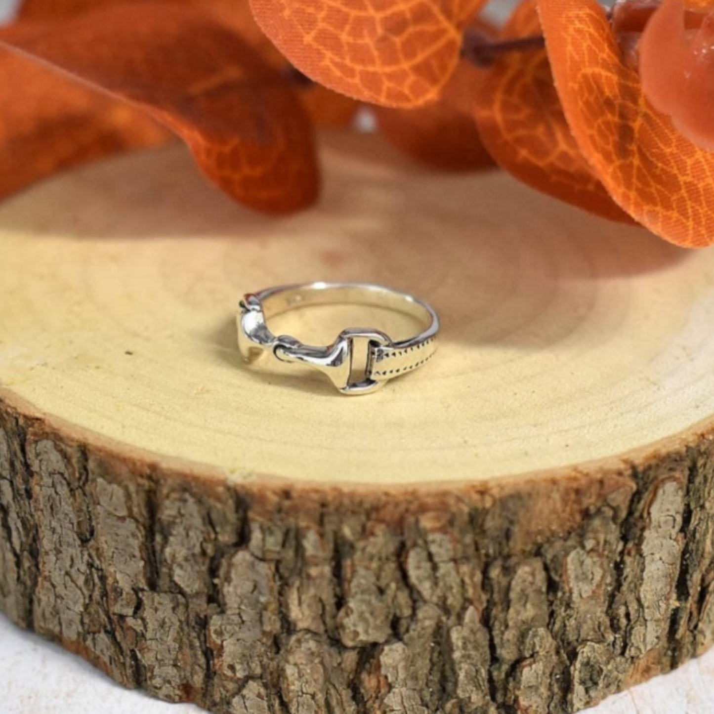Sterling silver snaffle ring inspired by equestrian tack displayed on a natural wooden slice.