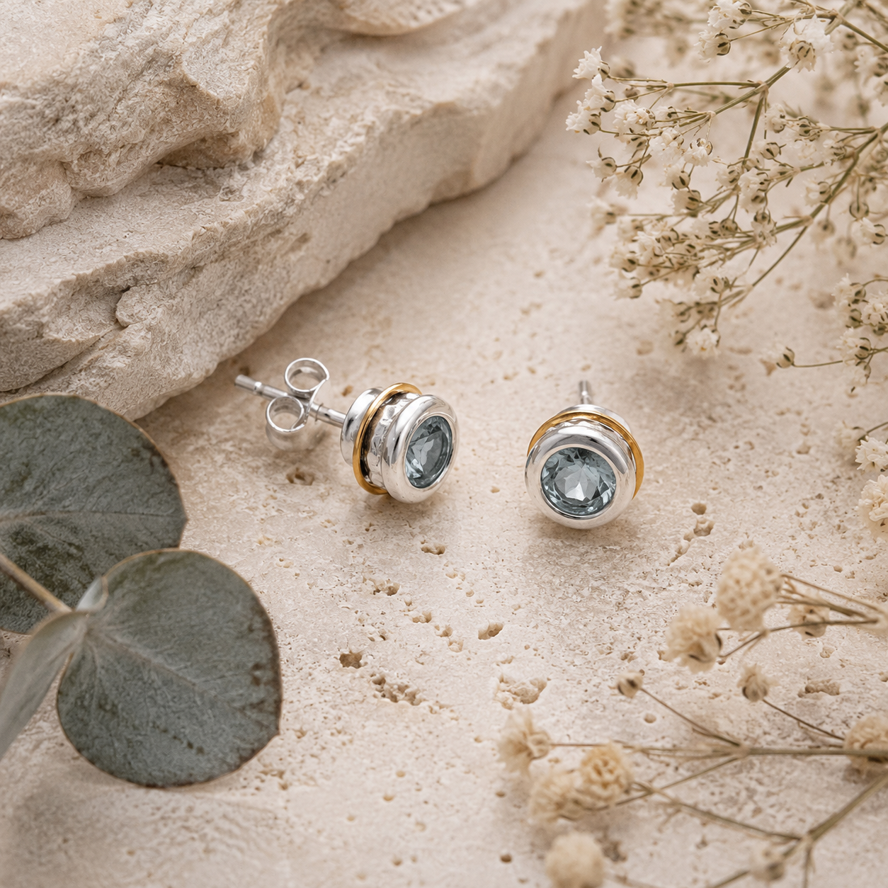 Sky Blue Topaz sterling silver and gold stud earrings styled on natural stone with botanical details