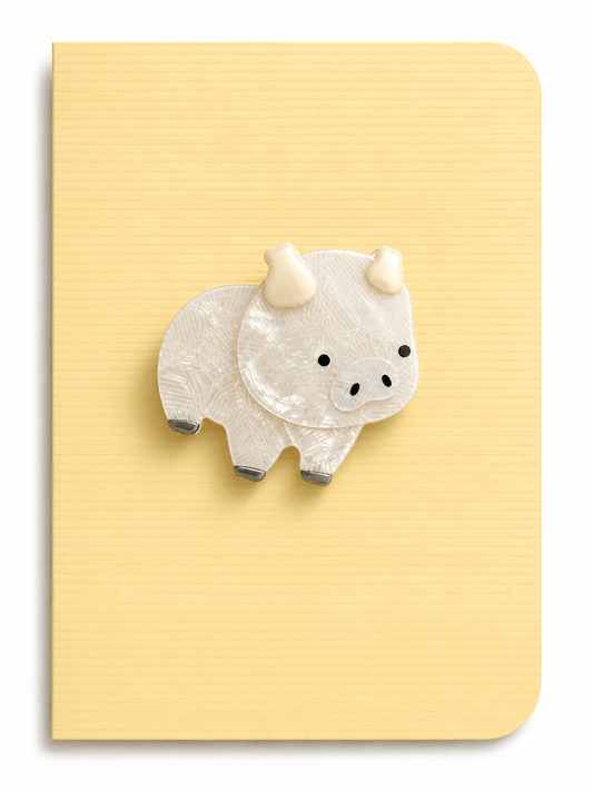 Cute pig brooch greeting card featuring a glossy pearlescent pig design mounted on a soft yellow ribbed card background.